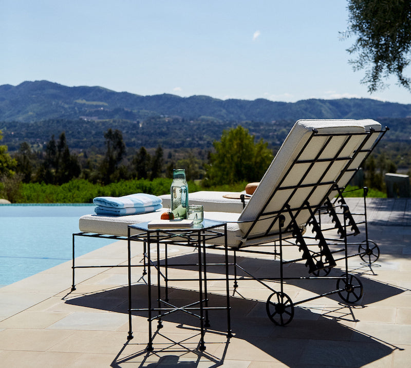 Main Image Outdoor seating with black metal frames and white cushions on a wooden deck, overlooking a green hillside.