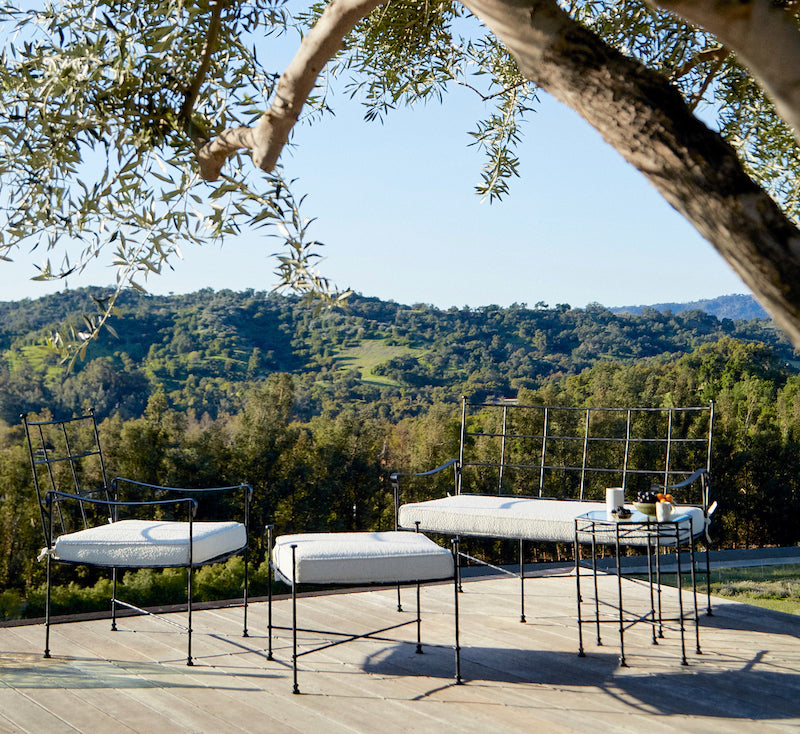 Main Image Outdoor seating with black metal frames and white cushions on a wooden deck, overlooking a green hillside.