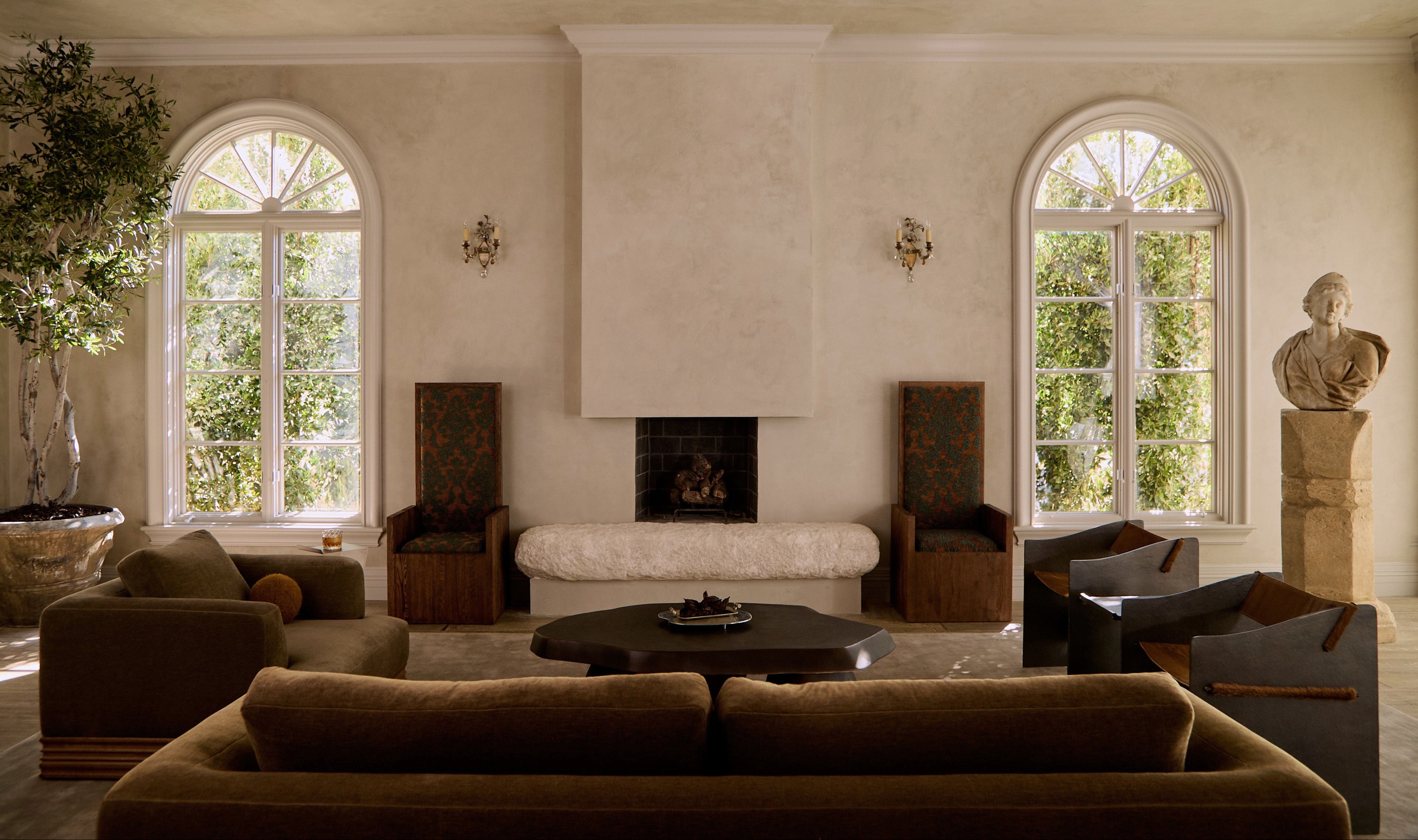 Main Image Living room featuring a cozy couch, sculptural coffee table, elegant chairs, and large windows with greenery outside.