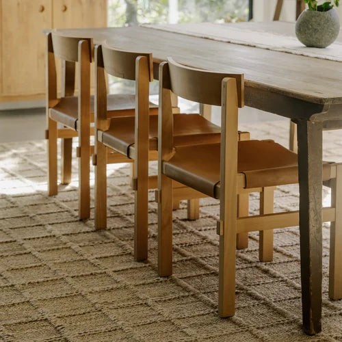 Wooden dining table with matching chairs in a sunlit room, decorated with ceramic vases and minimalist artwork.