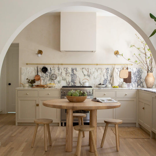 Modern kitchen with arched entry, marble backsplash, wood cabinets, and a round dining table with stools.