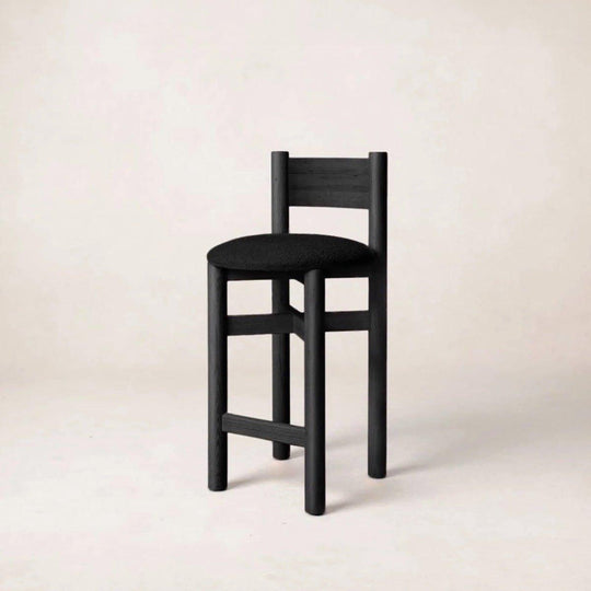 One black bar stools at a light wood kitchen island with a modern stove and neutral-toned backsplash in the background.