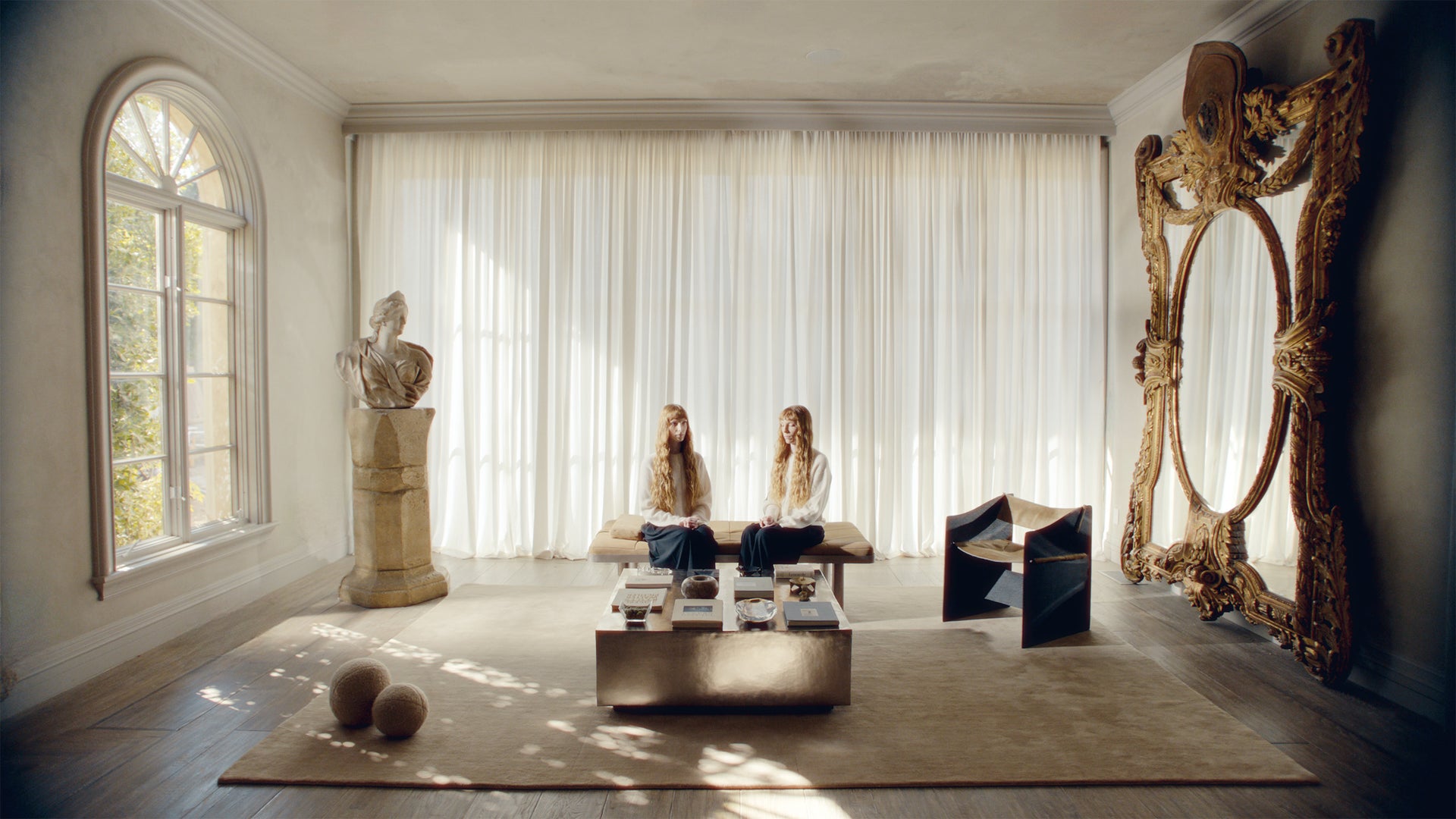 Two women sitting on a bench in a stylish room with large mirrors and decorative elements.