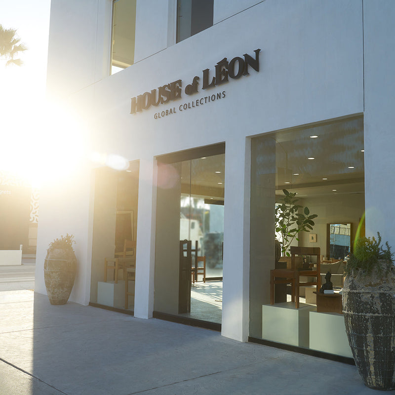 House of León storefront with large glass windows, modern white exterior, and decorative planters.
