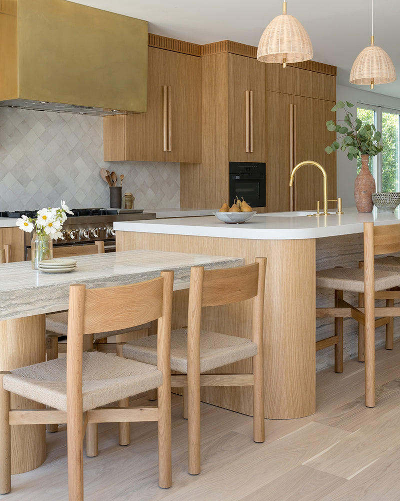 Modern kitchen with wooden cabinetry, a marble island, woven pendant lights, and wooden bar stools.
