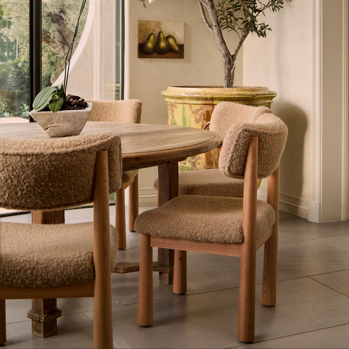 Dining room with wooden table and chairs, large window, and decorative plant.