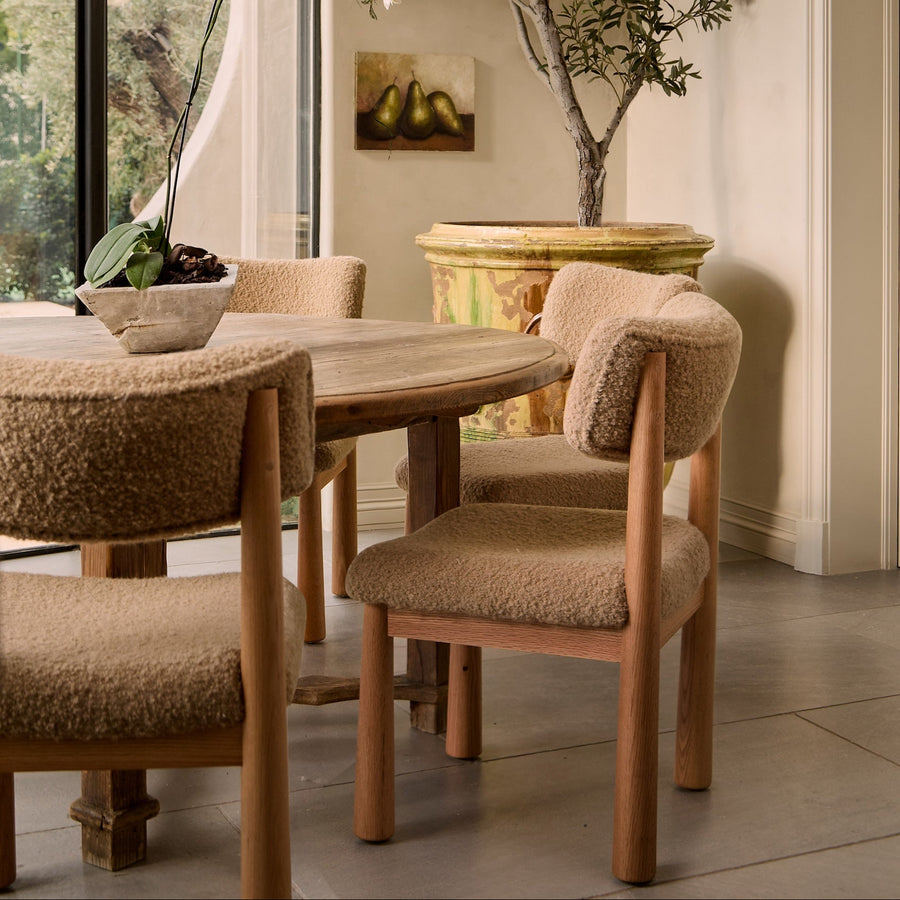 Dining room with wooden table and chairs, large window, and decorative plant.